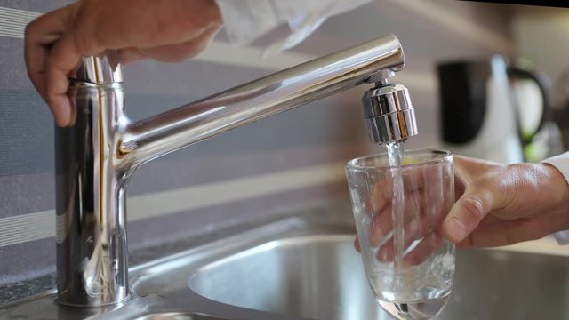 Pouring Fresh Tap Water Into a Glass - Close up of man hands, pouring glass of fresh water from tap in kitchen