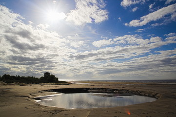 A medium sized water puddle beach sand sea clouds sunny