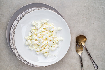 Homemade cottage cheese on a white plate on a gray background