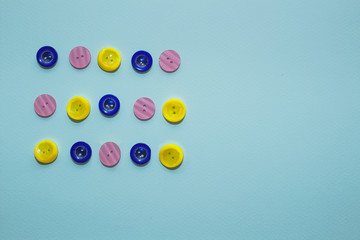 collection of various multicolored sewing button on blue background. Yellow, purple, dark blue buttons. Minimalism. Sewing accessories. Flatlay, place for text