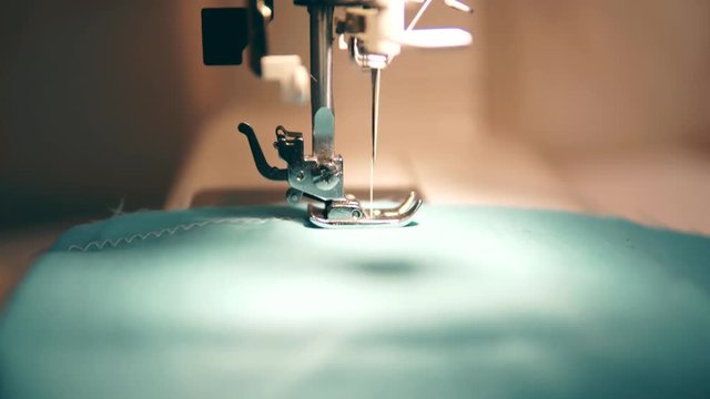 Sewing machine works with turquoise fabric. Close-up