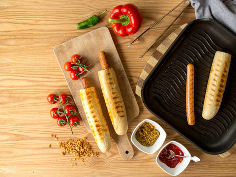 Hot dogi leżące w otoczeniu dodatk&oacute;w na patelni