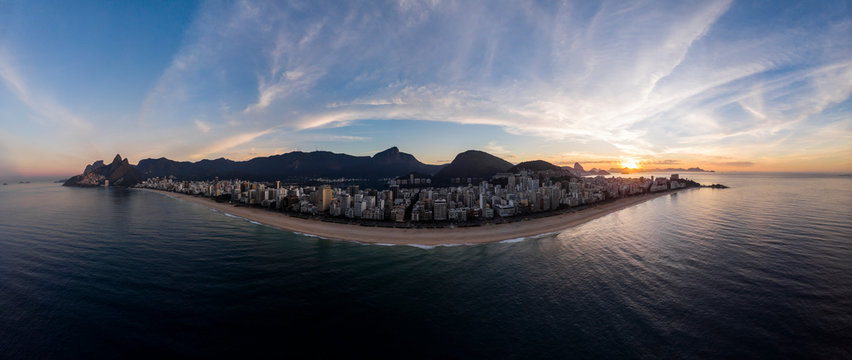 Aerial panorama of Rio de Janeiro with Ipanema and Leblon beach in the foreground and the wider cityscape in the background against a colourful blue sky at sunrise
