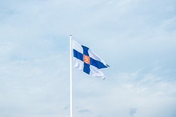 State flag of Finland with national coat of arms against blue sky