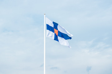 State flag of Finland with national coat of arms against blue sky