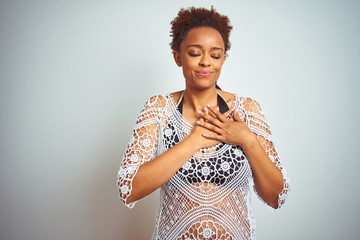 Young african american woman with afro hair wearing a bikini over white isolated background smiling with hands on chest with closed eyes and grateful gesture on face. Health concept.