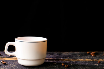 White coffee mug on wooden table and black background with space for text. Composition for coffee shop and coffee making