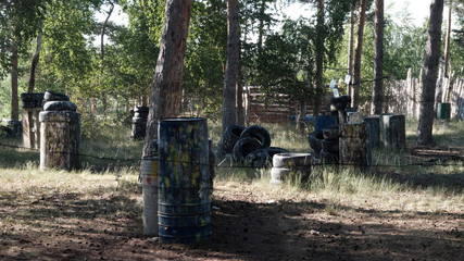 Paintball. Fenced area in the forest for the game of war. Old barrels and tires as shelters for players. Summer background. Sports team entertainment.