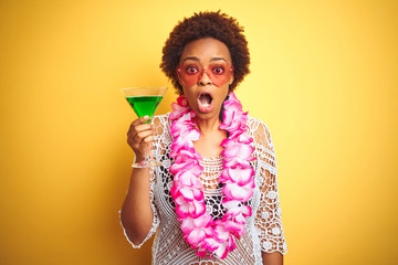 Young african american woman with afro hair wearing flower hawaiian lei and drinking a cocktail...