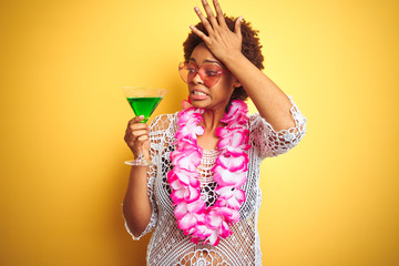 Young african american woman with afro hair wearing flower hawaiian lei and drinking a cocktail...