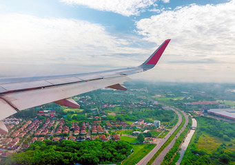 wings of airplane during the flight look from the passenger window. There are white clouds in the blue sky. Low flying above the ground, overlooking the clear city streets below Bangkok, Thailand