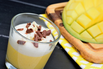 Mousse of mango fruit with whipped cream and chocolate in a glass jar on a wood table