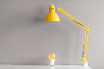 Glass of milk decorated with yellow bowtie standing on table under yellow lamp