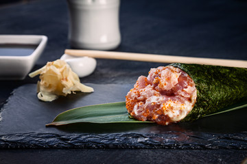 Close-up of tasty hand roll sushi with tuna and Tobico caviar served on dark stone plate with soy sauce and ginger. Copy space. Temaki, Japanese cuisine. Healthy food