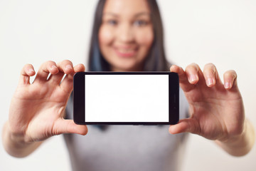 A nice woman holding a smartphone with an empty white screen with two hands horizontally and smiling On white background
