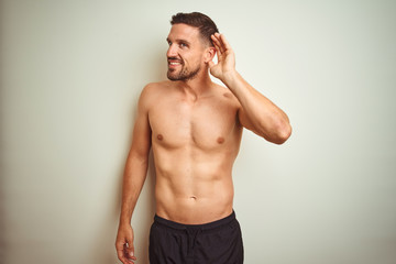 Fototapeta premium Young handsome shirtless man over isolated background smiling with hand over ear listening an hearing to rumor or gossip. Deafness concept.