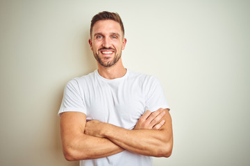 Obraz premium Young handsome man wearing casual white t-shirt over isolated background happy face smiling with crossed arms looking at the camera. Positive person.