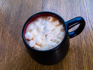Black mug with drink and marshmallows on a wooden surface