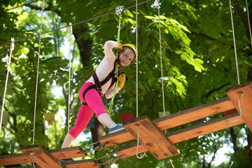 Little child climbing in adventure activity park with helmet and safety equipment. Happy child climbing in the trees.