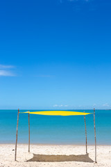 Beautiful beach view with a yellow tent on sunny summer day and sea and blue sky in the background. Concept of vacations, peace and relaxation. Ponta do Corumbau, Bahia, Brazil.