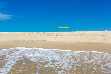 Fototapeta na wymiar Beautiful beach view from sea point of view and small yellow tent on sunny summer day. Blue sky in the background. Concept of vacations, peace and relaxation. Ponta do Corumbau, Bahia, Brazil.