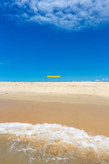 Beautiful beach view from sea point of view and small yellow tent on sunny summer day. Blue sky in the background. Concept of vacations, peace and relaxation. Ponta do Corumbau, Bahia, Brazil.