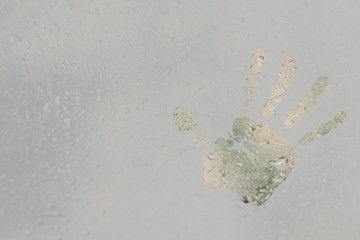 The imprint of a human palm on a translucent, misted glass. Spring rain drops on fogged window close up. blurred background copy space