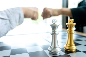 Businessman fist bump  near the chess board silver and gold color on the office desk.