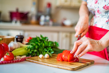 Female hand with knife slices bell pepper in kitchen. Cooking vegetables