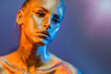 Fashion model woman golden skin face in bright sparkles, Trendy glowing gold skin make-up. Glitter metallic shine   makeup 