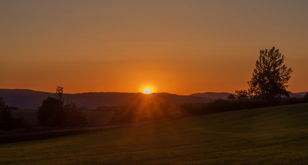 Fototapeta na wymiar Orange sunset on green grass field near Roprachtice village