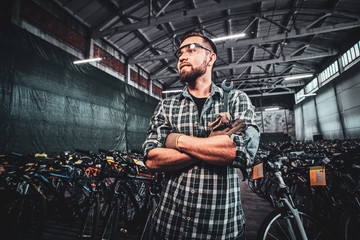 Fototapeta na wymiar Pensive handsome man crossed his hands is posing at mountain bycicles warehouse.