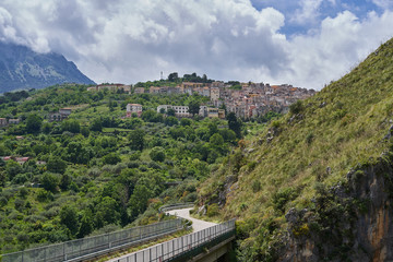 Fototapeta na wymiar Road and bridge over the wild creek to beautiful small mediaeval town Isnello to be located in Madonie mountain range in Italy in Palermo Province of Sicily. Picture is taken in cloudy spring day.