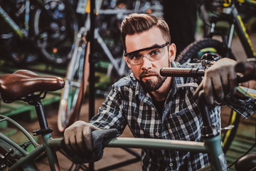 Happy attractive man in protective glasses and shirt is checkin bicycles chain for customer.