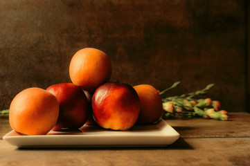 Peaches and apricots on a white plate, dark brown background