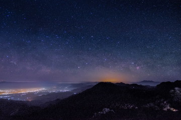 Mountain view morning at night of top hills and city around with soft fog under the stars in dark sky background, Monzone View Point Doi Ang Khang, Chiang Mai, northern of Thailand.