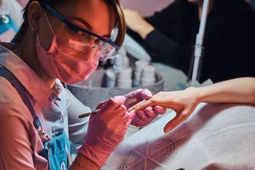 Beautiful cheerful manicure master is looking to camera while working on client's nails.