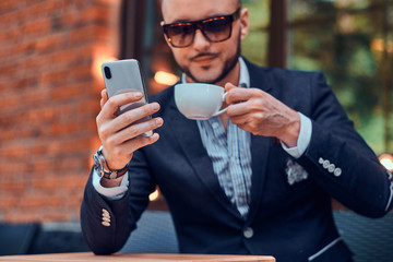 Serious sucessful man is calling by mobile phone while sitting outside coffeeshop enjoying his...