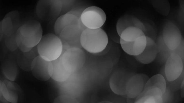 Black and white colors backdrop with soft motion of shiny particles. Abstract monochrome video of defocused Christmas holiday decorations isolated on black background.