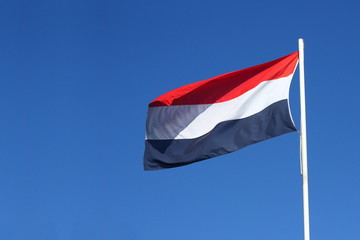 Fototapeta na wymiar Dutch flag waving in the wind at a sunny day with a clear blue sky