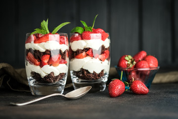 Trifles with fresh strawberries, chocolate biscuit and delicate cream on a dark background.