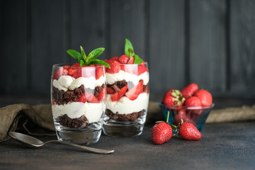 Trifles with fresh strawberries, chocolate biscuit and delicate cream on a dark background copy space.