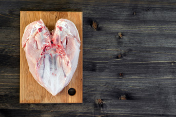 Chicken breast bones up lies on a bamboo cutting Board on a wooden rustic dark background.