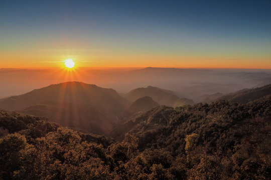Mountain view misty morning of top hills around with sea of fog with red and yellow sun light in the sky background, sunrise at Doi Ang Khang, Monzone view point, Chiang Mai, Thailand.