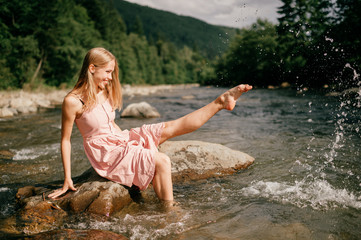Young happy girl kicking foot in river and splashing water.