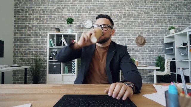 Crazy office worker is using laptop drinking coffee looking at camera concentrated on work then throwing carton glass and messing hair. Workaholics and job concept.