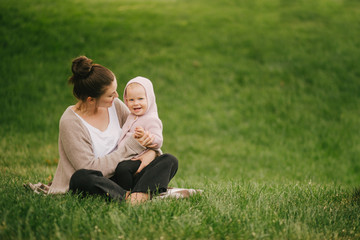 Fototapeta premium Young mother with her little baby daughter playing on fresh green grass in a park