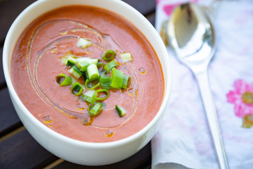 Traditional spanish vegan gazpacho presented on a wooden table with olive oil and fresh chopped cucumber and scallion