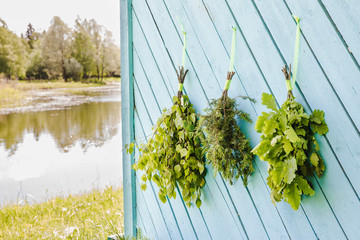 Fresh oak, birch, juniper and oak tree sauna whisks brooms hanging and drying on sauna house wall by beautiful natural lake. Traditional Finnish sauna concept.