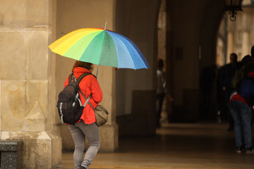 A girl in bright autumn clothes with a large umbrella of all colors of the rainbow walks in the city in the rain. Gay parade of equality. Walk in rainy weather with a trendy gadget. Melancholic